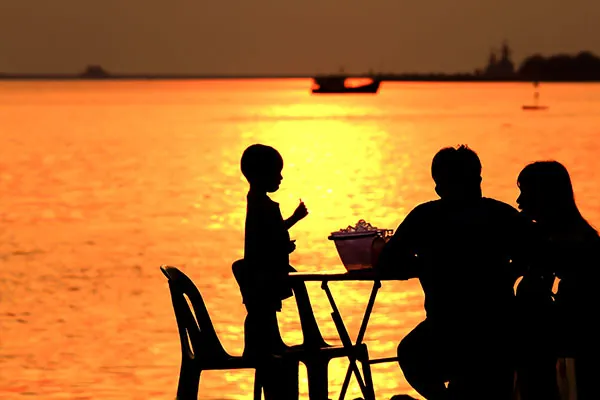 Sagome di una famiglia a cena in riva al mare al tramonto